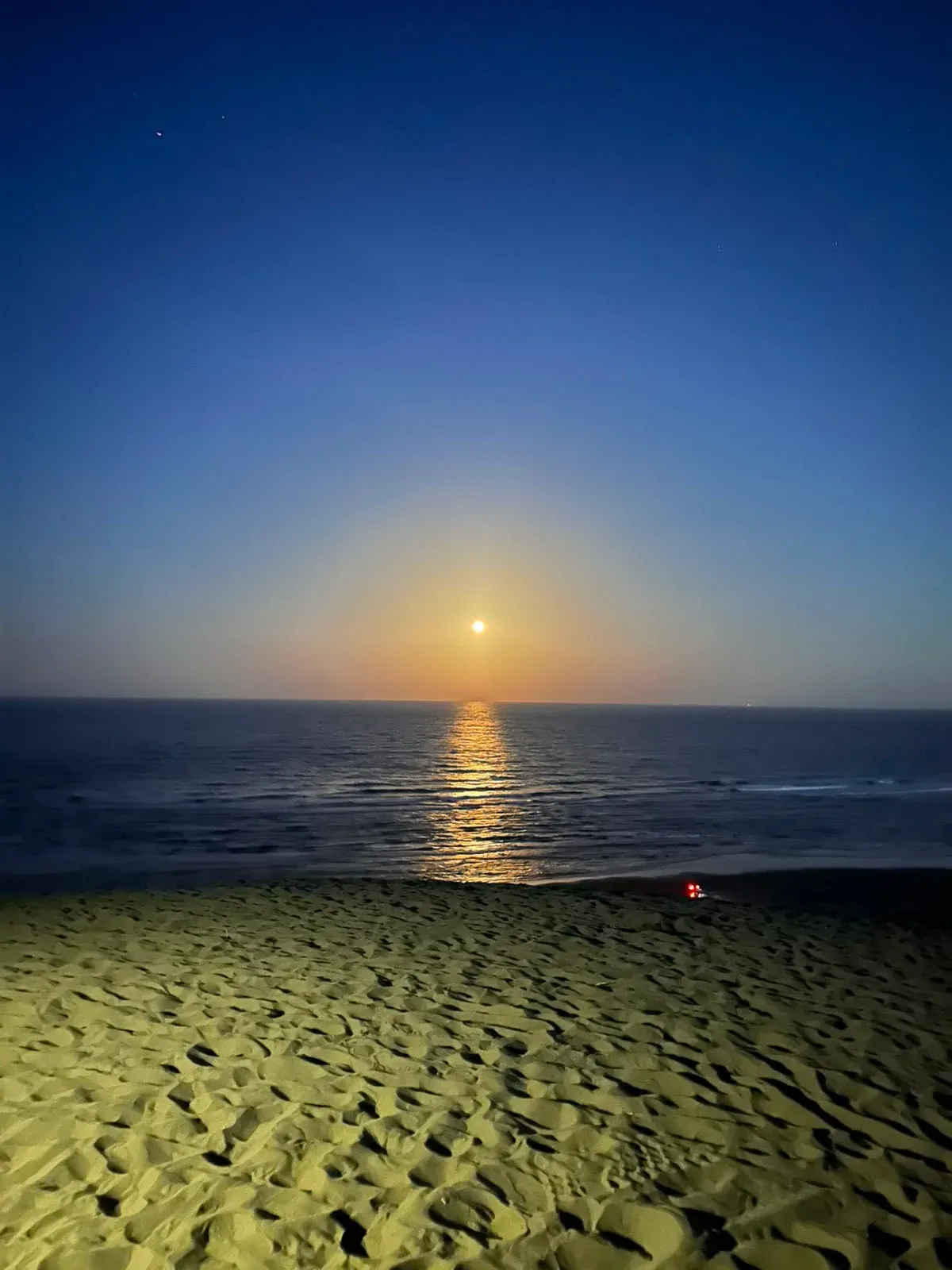 La luna saliendo sobre el mar al anochecer, vista desde la playa